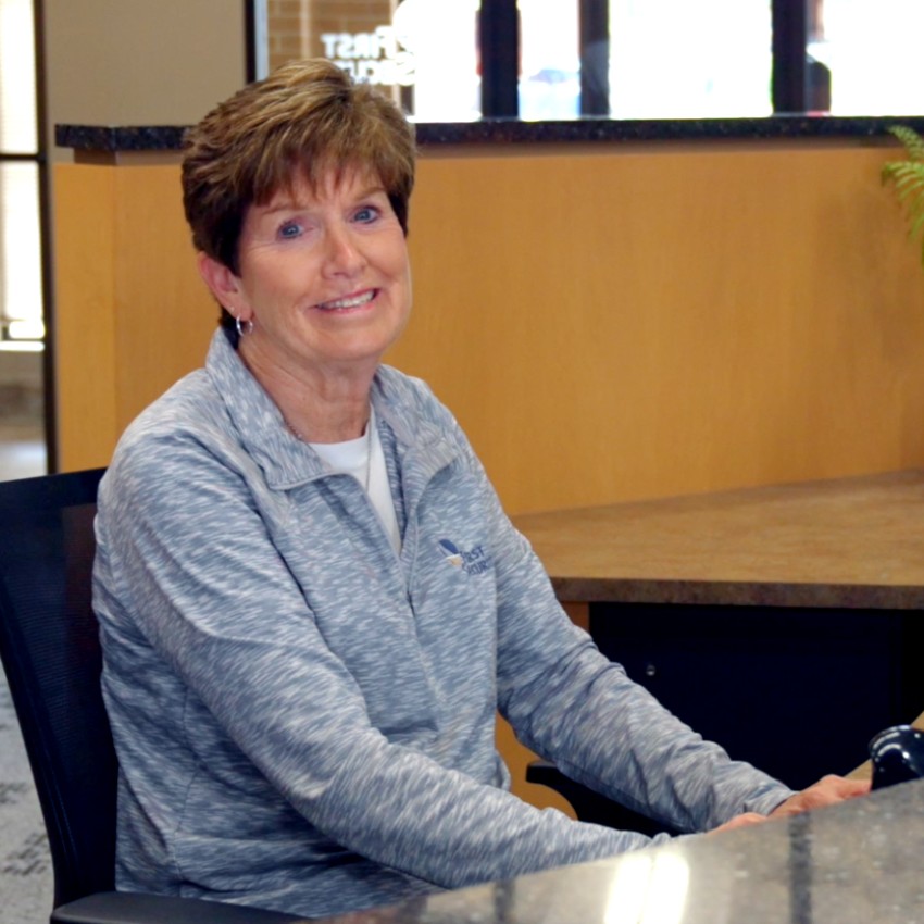 First Security employee smiling behind desk in bank lobby.