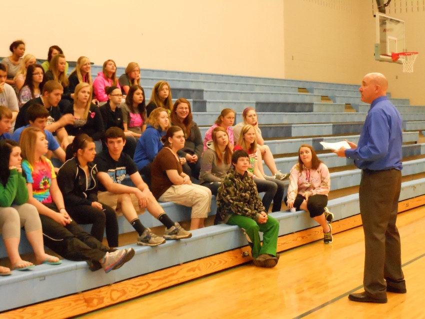 Randy presenting on financial literacy in front of bleachers full of students.